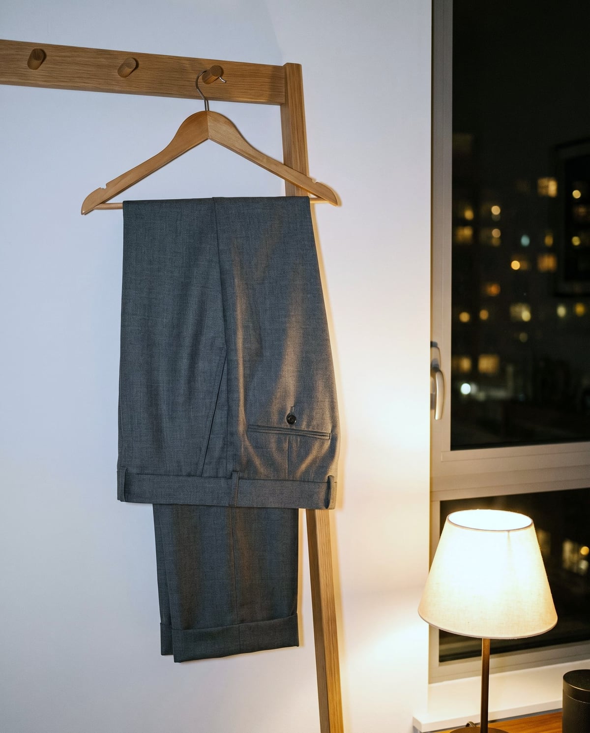 夜の部屋で、ハンガーに吊るしたグレーのパンツ