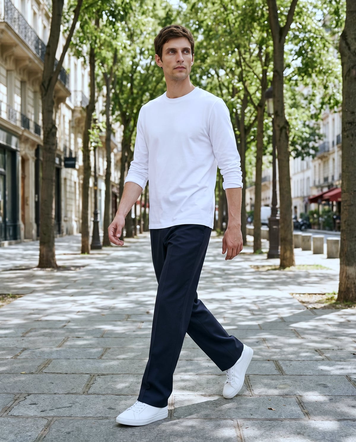 昼、街路樹の歩道を歩く、白いロングスリーブTシャツにネイビーのストレートの男性