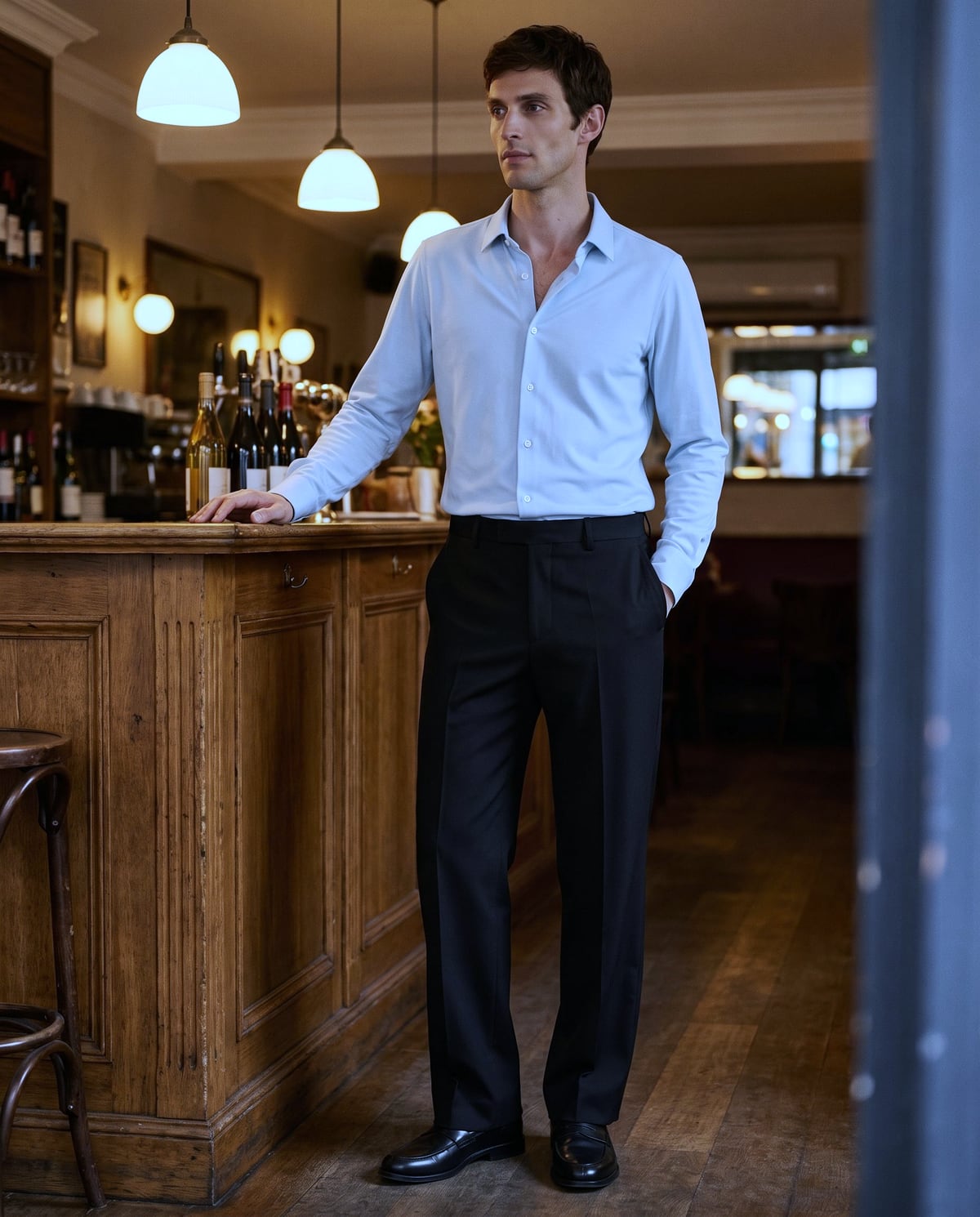 夜、ビストロのカウンターの横に立つ、淡いブルーのシャツにブラックのストレートの男性