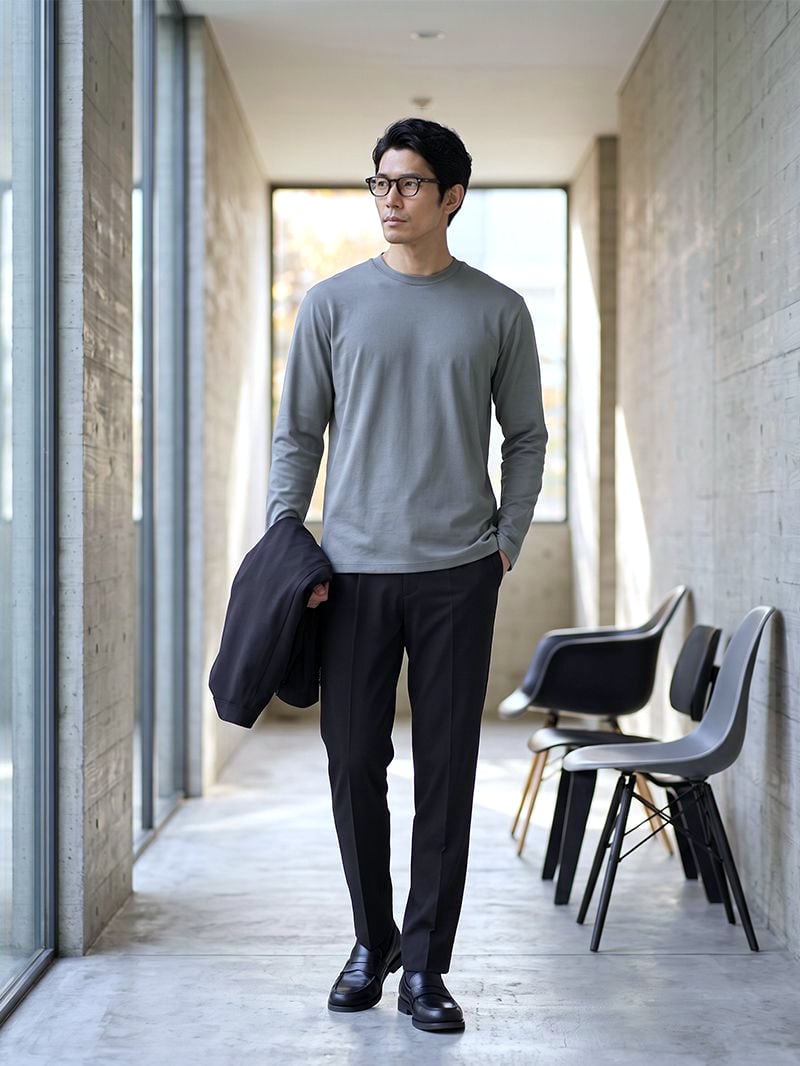 ブラックのパンツにグレーのカットソー。ジャケットを手に持って廊下を歩く