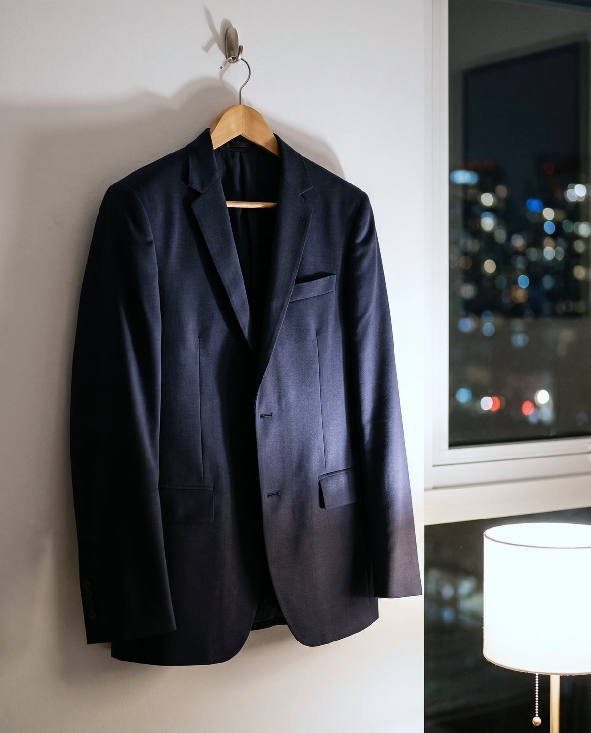 夜の部屋で、壁のフックにハンガーで吊るしたネイビーのジャケット