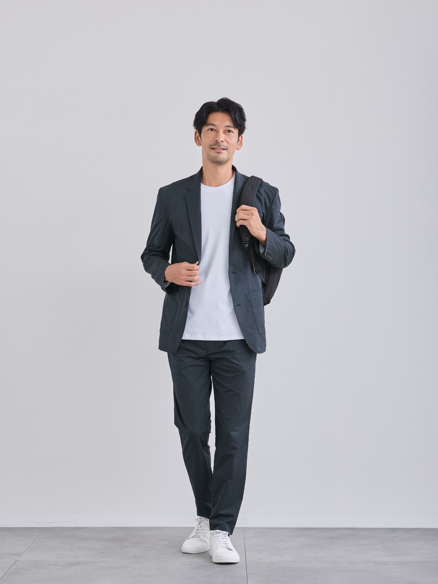 同じセットアップにリュックとスニーカーを合わせて移動する40代男性