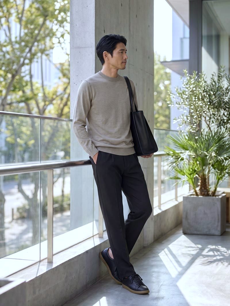 グレージュのCODEシルクニットにブラウンのパンツ、トートバッグを持った男性