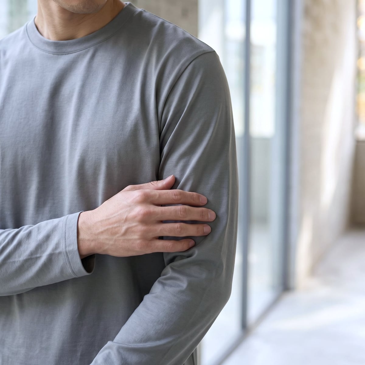 グレーのCODEロングスリーブTシャツの袖に手を添えて、生地のなめらかさを確かめているところ