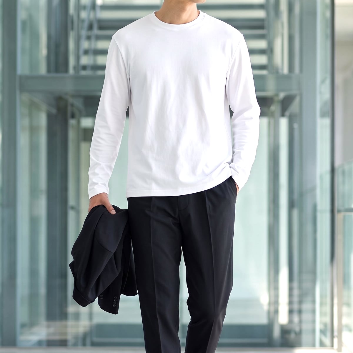 白のCODEロングスリーブTシャツにブラックのパンツ、ジャケットを手に持った男性の胴まわり