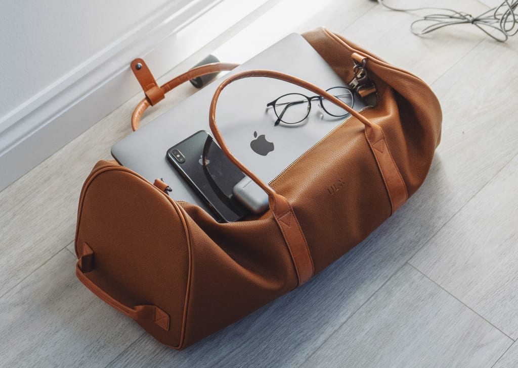茶色のボストンバッグの上にのったパソコンやメガネ