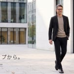 秋の服は、セットアップから。AUTUMN STYLING 2026。黒のCODEジャケットとCODEイージーパンツに、グレージュのCODEシルクニットを合わせて朝のオフィス街を歩く男性