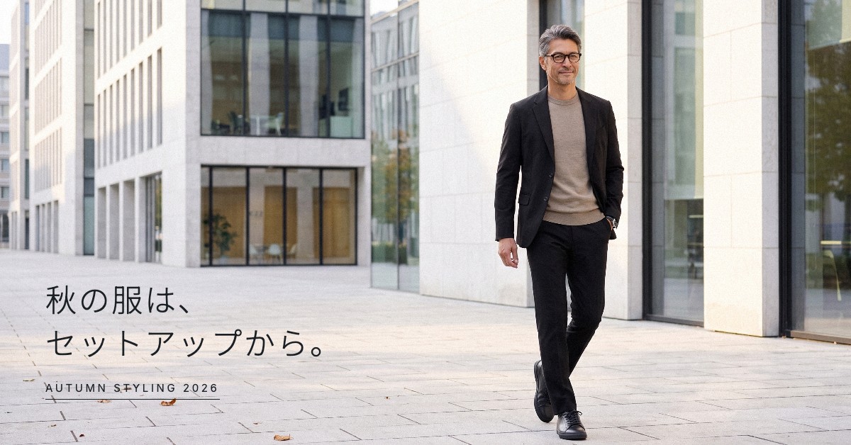 秋の服は、セットアップから。AUTUMN STYLING 2026。黒のCODEジャケットとCODEイージーパンツに、グレージュのCODEシルクニットを合わせて朝のオフィス街を歩く男性