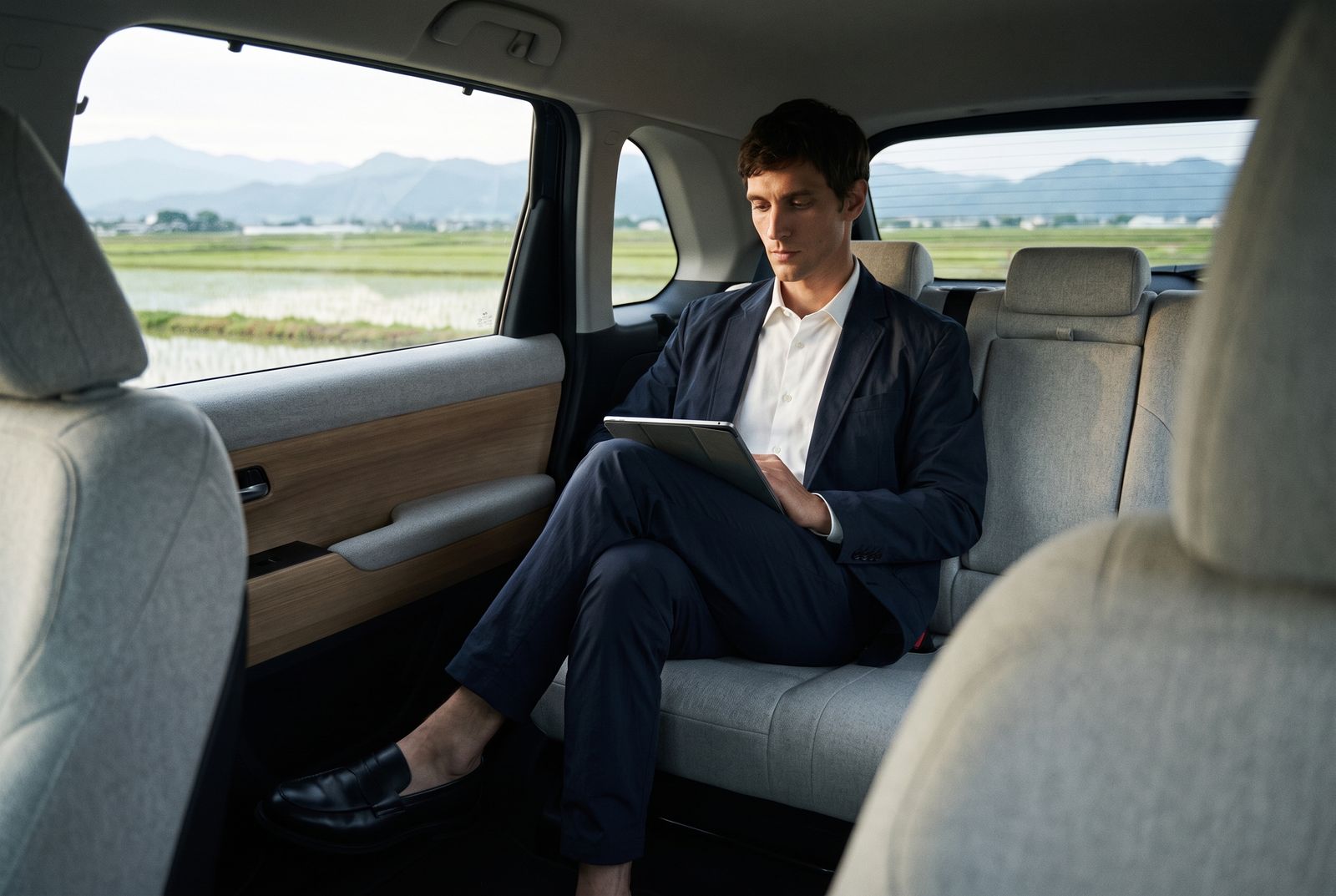 ハンドルのない自動運転の車内で、脚を組んでタブレットを読む男性